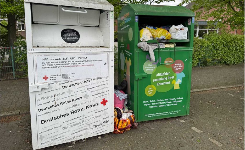 Überfüllter Altkleidercontainer mit abgestellten Säcken und alter Kleidung.